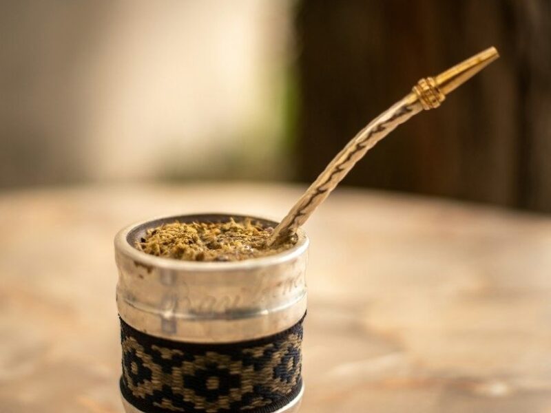 Traditioneller Mate-Becher mit Kräuteraufguss und Bombilla auf einem Holztisch