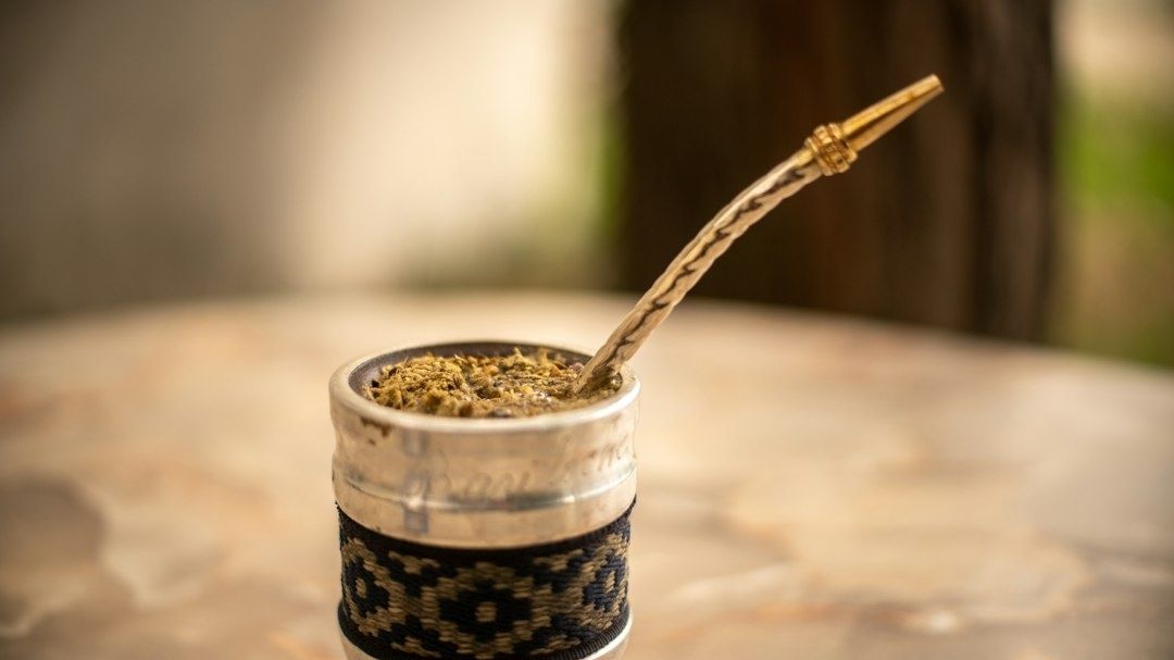 Traditioneller Mate-Becher mit Kräuteraufguss und Bombilla auf einem Holztisch